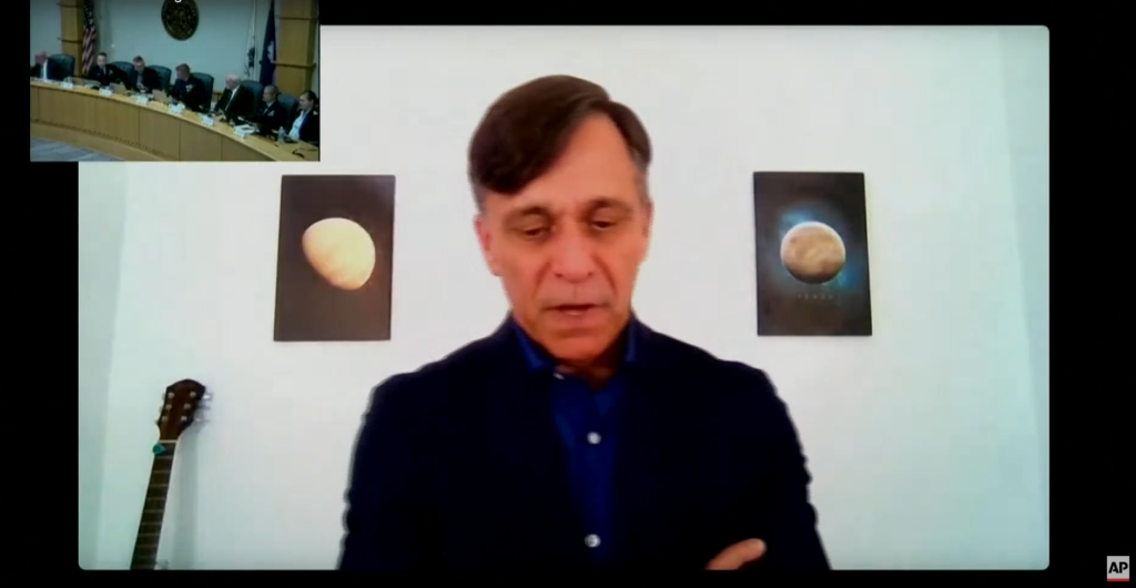 Guillermo Sohnlein, cofundador de OceanGate, testificando de manera remota ante un panel de la Guardia Costera de los Estados Unidos. En la esquina superior izquierda de la imagen, se puede ver al panel de oficiales de la Guardia Costera sentados en una sala de audiencias, mientras que Sohnlein aparece en primer plano desde una videollamada, hablando en lo que parece ser una oficina o habitación. Detrás de él hay dos cuadros en la pared que muestran imágenes espaciales, y a un lado, una guitarra apoyada contra la pared.