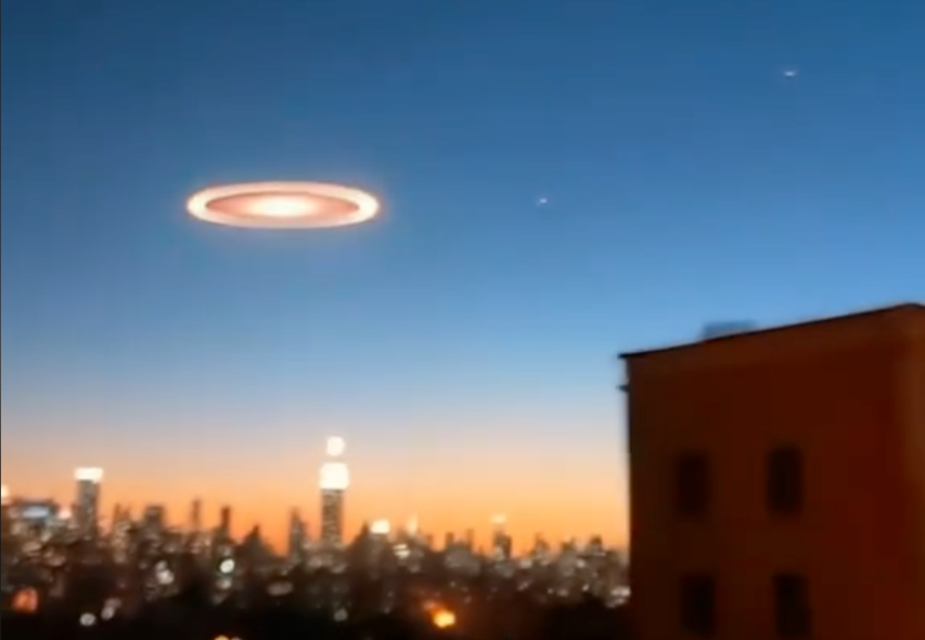 Una imagen que muestra un horizonte urbano al atardecer, con un cielo azul degradado hacia tonos anaranjados. En el centro del cielo, se ve un objeto circular brillante con un anillo luminoso, que parece suspendido sobre la ciudad. El paisaje incluye edificios y luces que destacan en la oscuridad creciente, con un rascacielos iluminado en el centro de la escena.