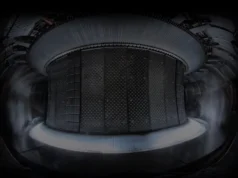 Francia establece un nuevo récord al mantener reactor de fusión funcionando durante 22 minutos Interior de un reactor de fusión nuclear tipo Tokamak. Se observa una estructura cilíndrica metálica con paneles diseñados para resistir temperaturas extremas. En la parte inferior, un resplandor brillante indica la presencia de plasma de alta energía. Vapor o gas rodea la estructura, posiblemente como parte del sistema de enfriamiento o control del ambiente dentro del reactor. La iluminación tenue y el diseño industrial refuerzan la sensación de una instalación científica avanzada.