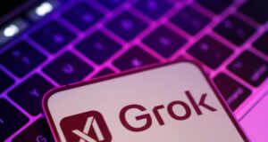 Teléfono móvil con el logo de Grok, el chatbot de inteligencia artificial de xAI, sobre un teclado iluminado con luces en tonos morados y rosados.