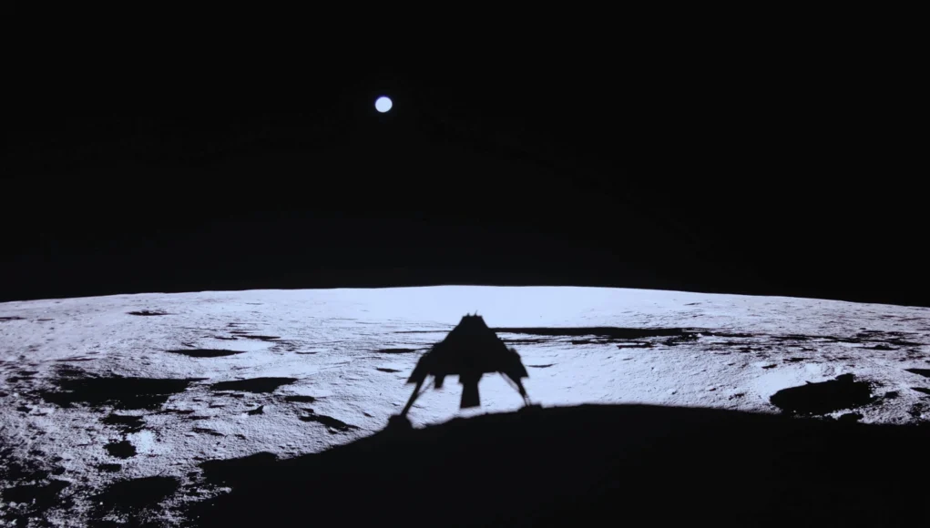 Sombra del módulo de aterrizaje Blue Ghost proyectada sobre la superficie lunar, con el horizonte iluminado y la Tierra visible como un punto brillante en el cielo.