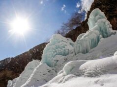 Glaciares artificiales impulsan el suministro de agua en el norte de Pakistán Formaciones de hielo y nieve en una ladera montañosa bajo un cielo despejado, con el sol brillando intensamente y árboles sin hojas al fondo, creando un contraste entre el clima frío y la luz solar.
