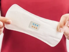 El primer dispositivo del mundo que detecta cáncer y enfermedades usando sangre menstrual Primer plano de una persona sosteniendo una compresa blanca con un sensor integrado que muestra indicadores de colores, posiblemente diseñado para monitorear la salud o detectar infecciones.