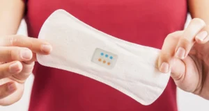 Primer plano de una persona sosteniendo una compresa blanca con un sensor integrado que muestra indicadores de colores, posiblemente diseñado para monitorear la salud o detectar infecciones.