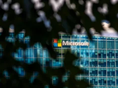 Microsoft firma contrato para enterrar 4.9 millones de toneladas de desechos orgánicos para compensar emisiones de IA Vista parcial de la sede de Microsoft a través de hojas desenfocadas en primer plano, mostrando el logo de la compañía en un edificio moderno de cristal azul.