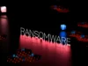 Palabra 'RANSOMWARE' iluminada sobre un fondo oscuro con una rejilla digital y luces rojas y azules.