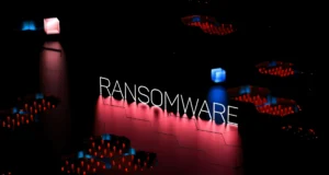 Palabra 'RANSOMWARE' iluminada sobre un fondo oscuro con una rejilla digital y luces rojas y azules.