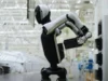 Walker S2: El robot humanoide que cambia sus propias baterías Robot humanoide de color blanco y negro realizando tareas frente a una máquina en una moderna fábrica automatizada, rodeado de estructuras industriales iluminadas con luz blanca.