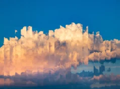 Cloudflare declara la guerra a los rastreadores de IA y bloquea por defecto el acceso web Nubes algodonosas de tonos cálidos sobre un cielo azul, con un efecto visual de repetición o distorsión digital que divide la imagen en columnas verticales, creando una apariencia fragmentada y artística del cielo.