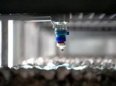 Una startup canadiense recibe 40 millones de dólares para automatizar la cosecha de hongos con IA Brazo robótico con ventosa recogiendo un champiñón en una granja de cultivo. El dispositivo mecánico cuelga del techo y utiliza succión para manipular el hongo, mientras en el fondo se observa una hilera difusa de otros champiñones en crecimiento.