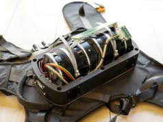 Una mochila giroscópica que ayuda a personas con ataxia a mantener el equilibrio Dispositivo mecánico y electrónico montado en una estructura de arnés con correas, que muestra cables de colores, ventiladores y componentes metálicos.