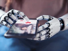 El ‘Chatfishing’ llega a las apps de citas: usuarios emplean ChatGPT para seducir con inteligencia artificial Manos robóticas sostienen un teléfono inteligente y tocan la pantalla en una aplicación de citas, sobre un ícono de corazón rojo, simbolizando la interacción de la inteligencia artificial con las relaciones humanas.