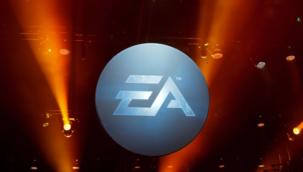 EA Stability AI Logotipo de Electronic Arts (EA) iluminado en un escenario oscuro con focos naranjas apuntando hacia arriba.