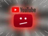 YouTube ofrece una segunda oportunidad a creadores baneados permanentemente, pero hay una trampa Logotipo de YouTube acompañado del ícono clásico de error con cara neutra en rojo, resaltado con un efecto dramático de rayos y destellos que irradian desde el centro sobre un fondo gris.