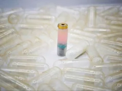 Dispositivo ingerible MEDS trata úlceras perforadas sin cirugía Cápsula médica experimental con sensores de colores en su interior, diseñada para monitorear el sistema digestivo, rodeada de cápsulas transparentes vacías.