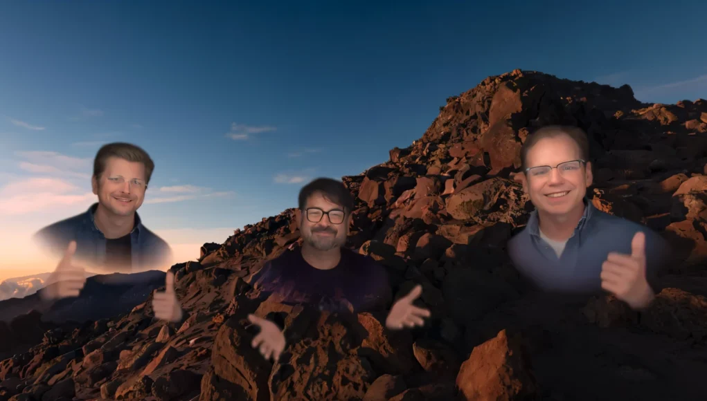 Apple Persona Tres avatares semitransparentes de hombres aparecen sobre un paisaje rocoso al atardecer; los tres están sonriendo, dos de ellos levantan los pulgares y el del centro gesticula con las manos.