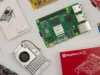 Desarrollador crea agente de IA local usando solo una Raspberry Pi 5 Varios componentes electrónicos dispuestos sobre una superficie clara, incluyendo una placa Raspberry Pi 5, cajas de embalaje, una unidad de refrigeración con ventilador y otras placas de expansión y accesorios.